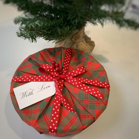 A sweet tin covered in red & green tartan giftwrap with a red and white spotty ribbon